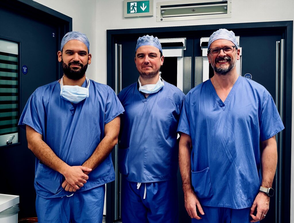 Surgeons Marios Theologu , Chris Barrett and Calan Mathieson in blue surgical scrubs.