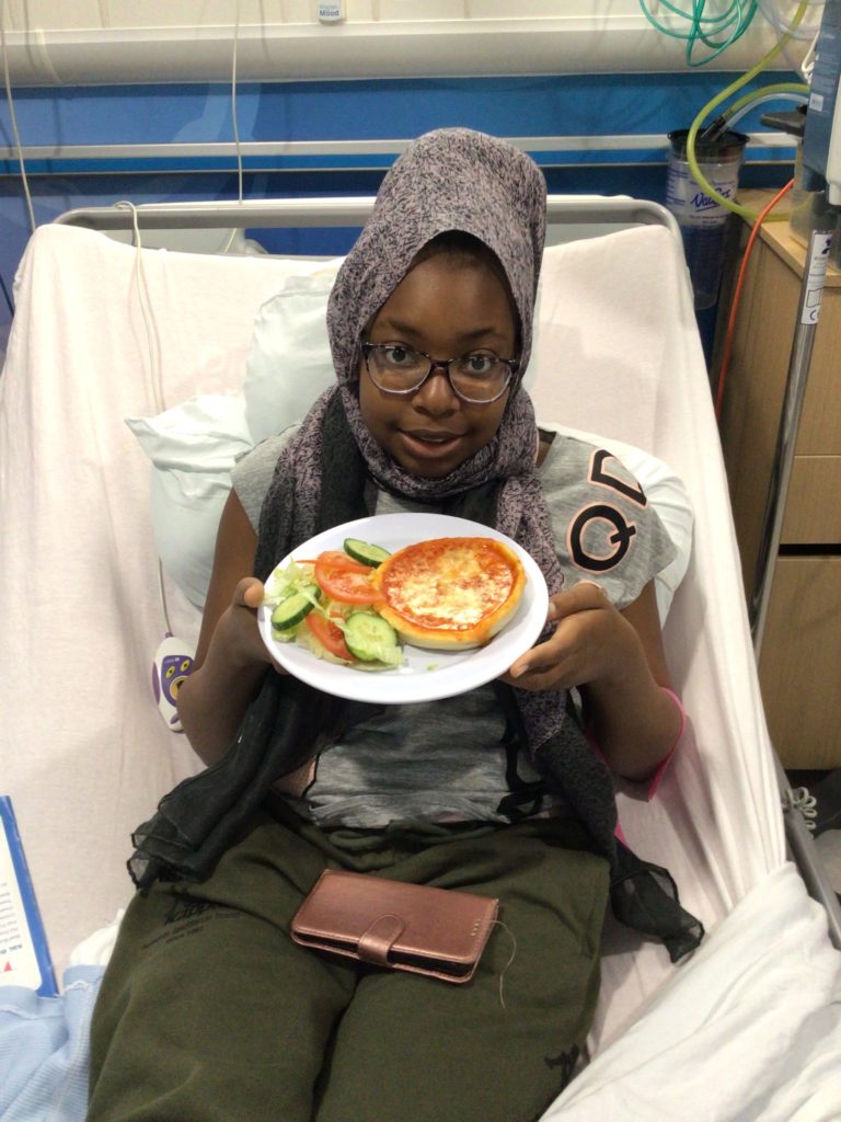 Young patient sits on hospital bed with plate containing pizza and salad