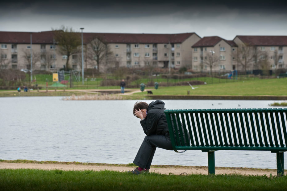 A depressed man sitting on a bench by a pond.