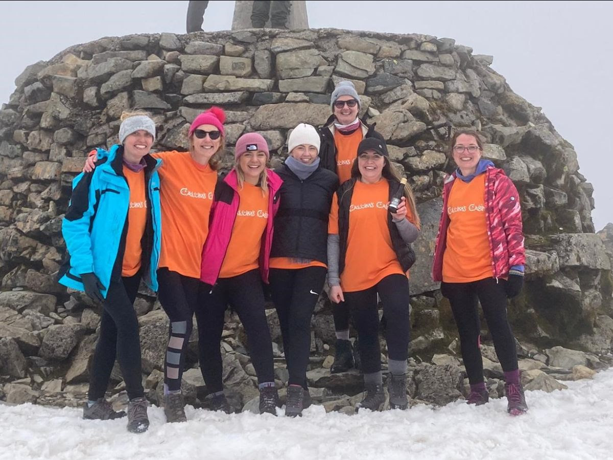 Seven members of the RHC team at the peak of a snow-covered Ben Nevis. They are smiling, wearing Calum's Cabin fundraising clothes.