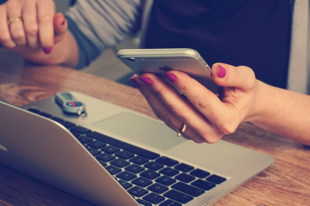 Woman looks at mobile phone in front of laptop