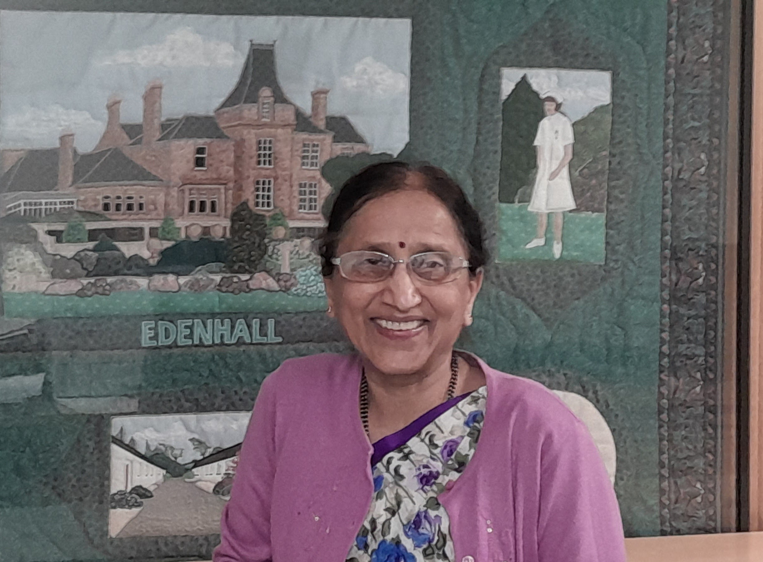 Dr Mahandra Verappa Jigajinni - affectionately known as Dr Jig - smiling with tapestry of Edenhall Hpspital in background