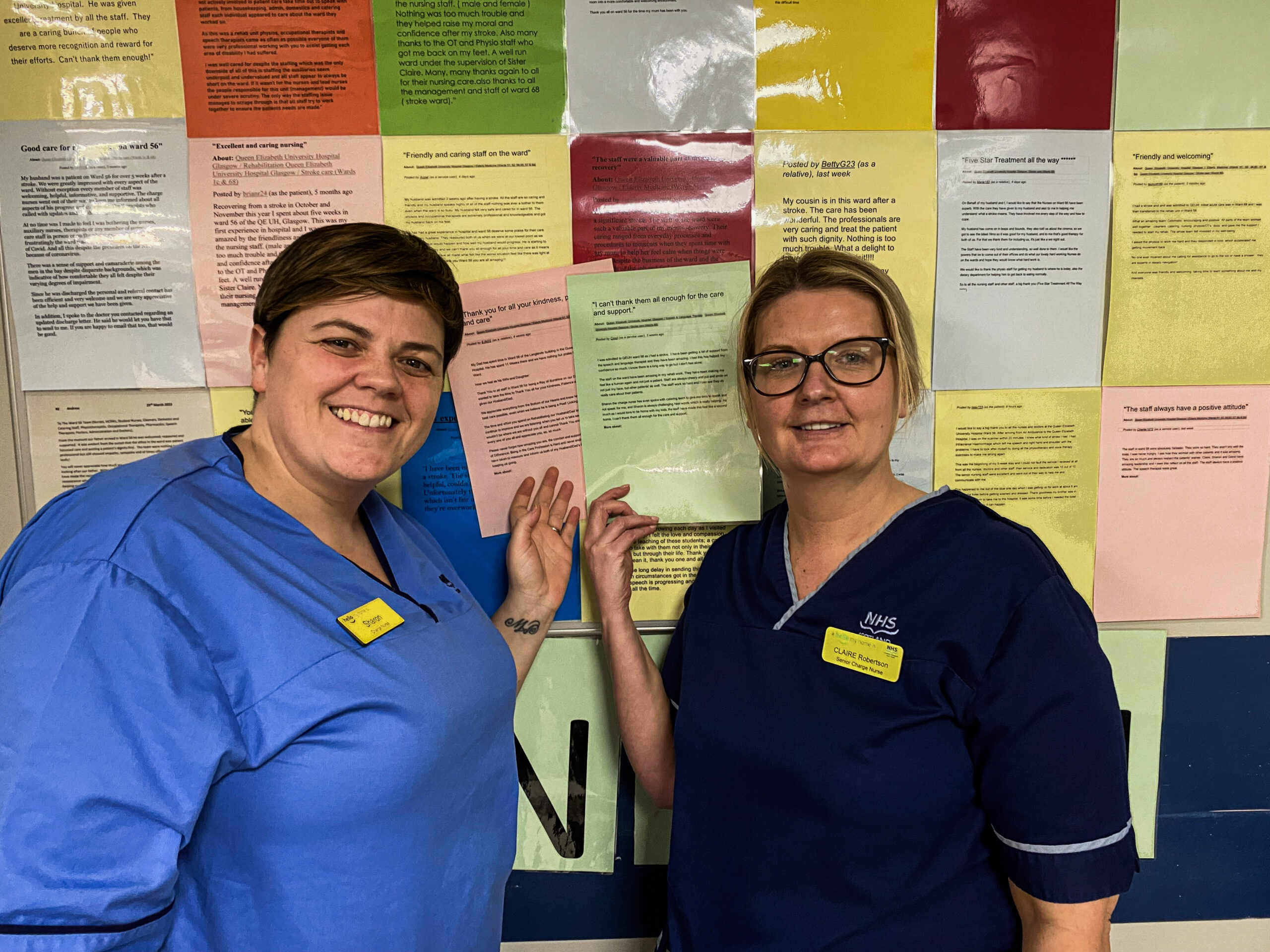 Two smiling nurses stand beside a board displaying dozens of messages of thanks from former patients and relatives.