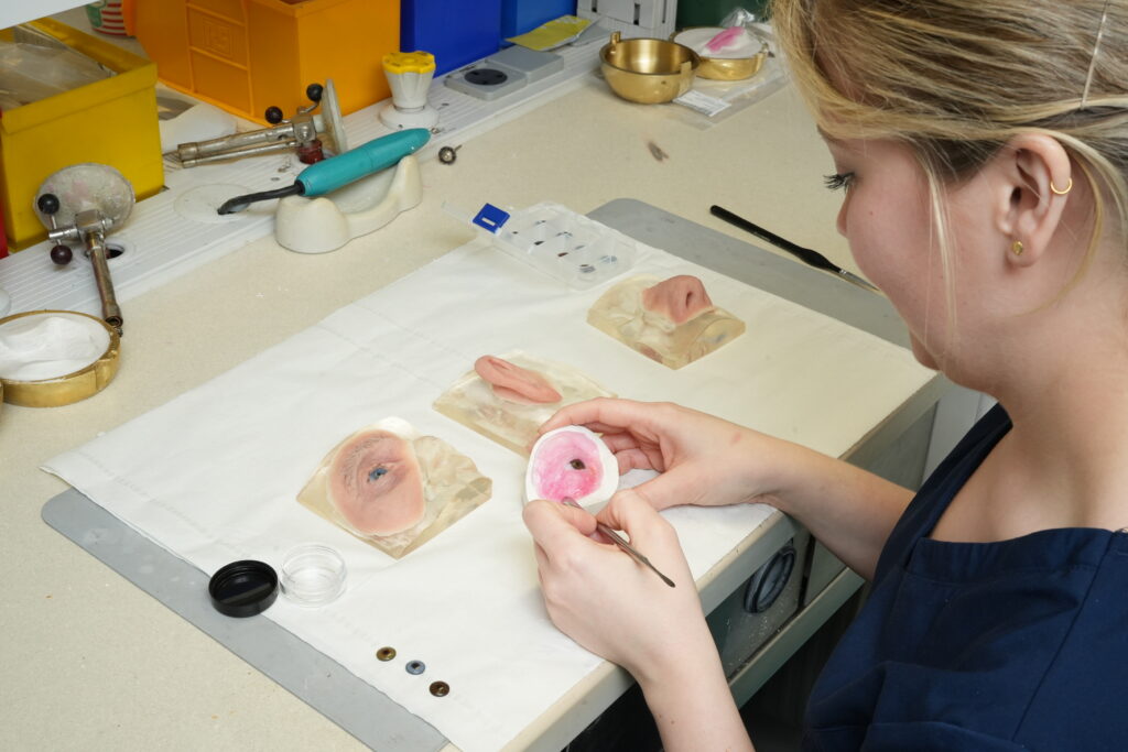 Danielle Adair uses a painting brush to finish off a prosthetic for a patient.