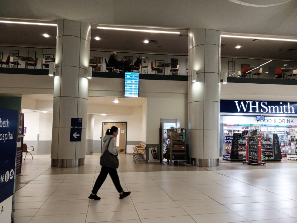 Woman walking through atrium of the QEUH, with one off the new real-time information screens in place beside her.