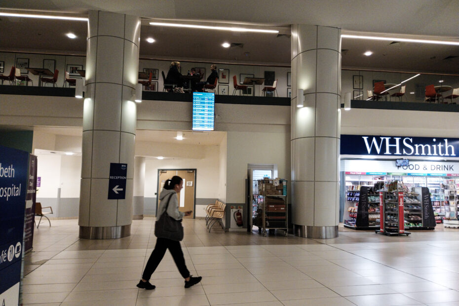 Woman walking through atrium of the QEUH, with one off the new real-time information screens in place beside her.