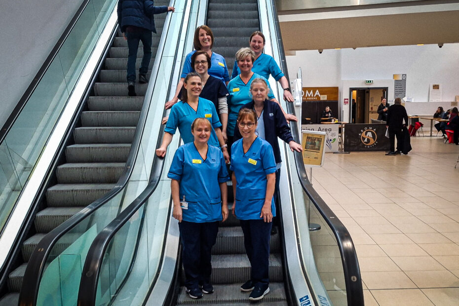 Member of the New Victoria Hospital Parkinson's team gathered on an escalator in the atrium of the hospital