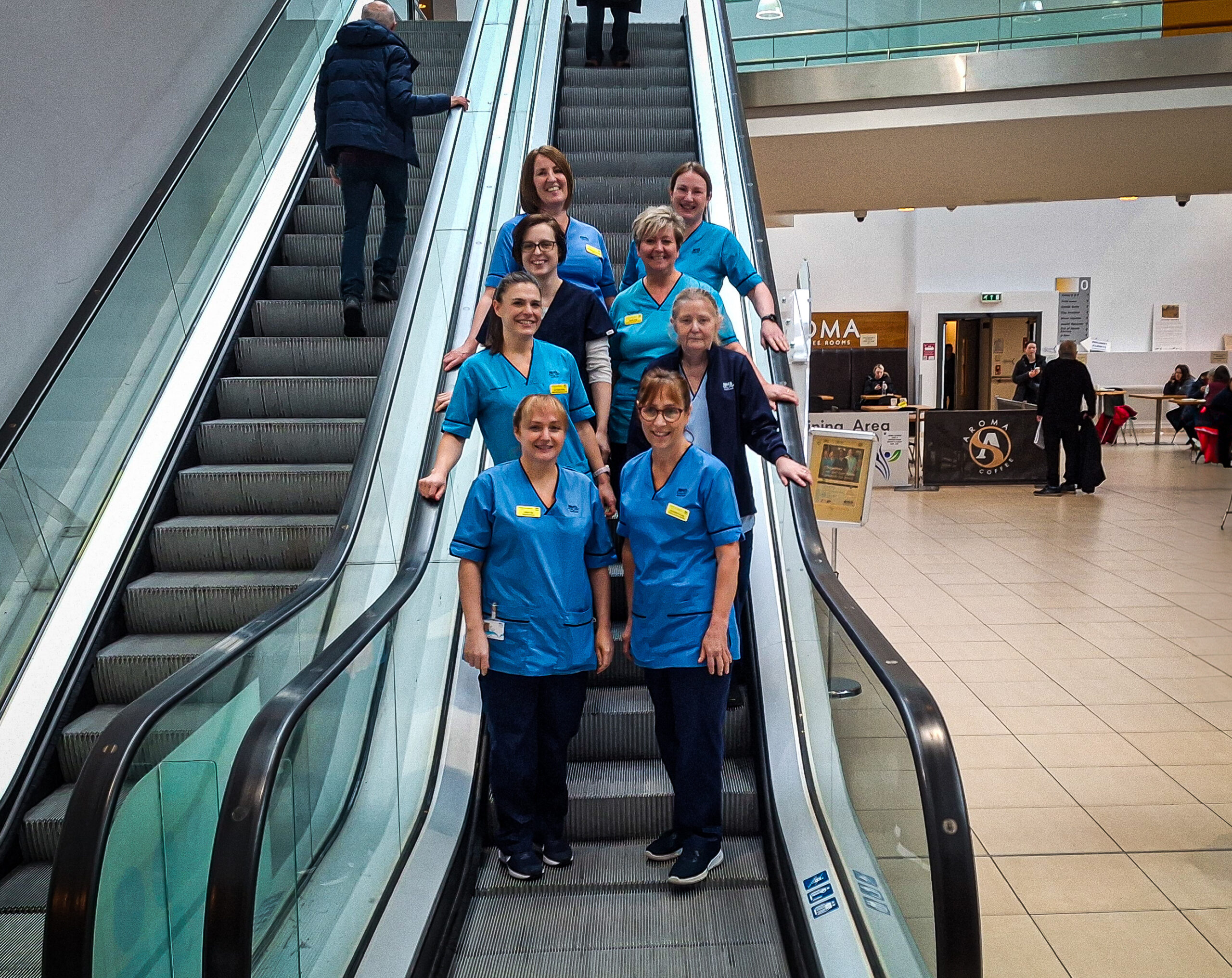 Member of the New Victoria Hospital Parkinson's team gathered on an escalator in the atrium of the hospital