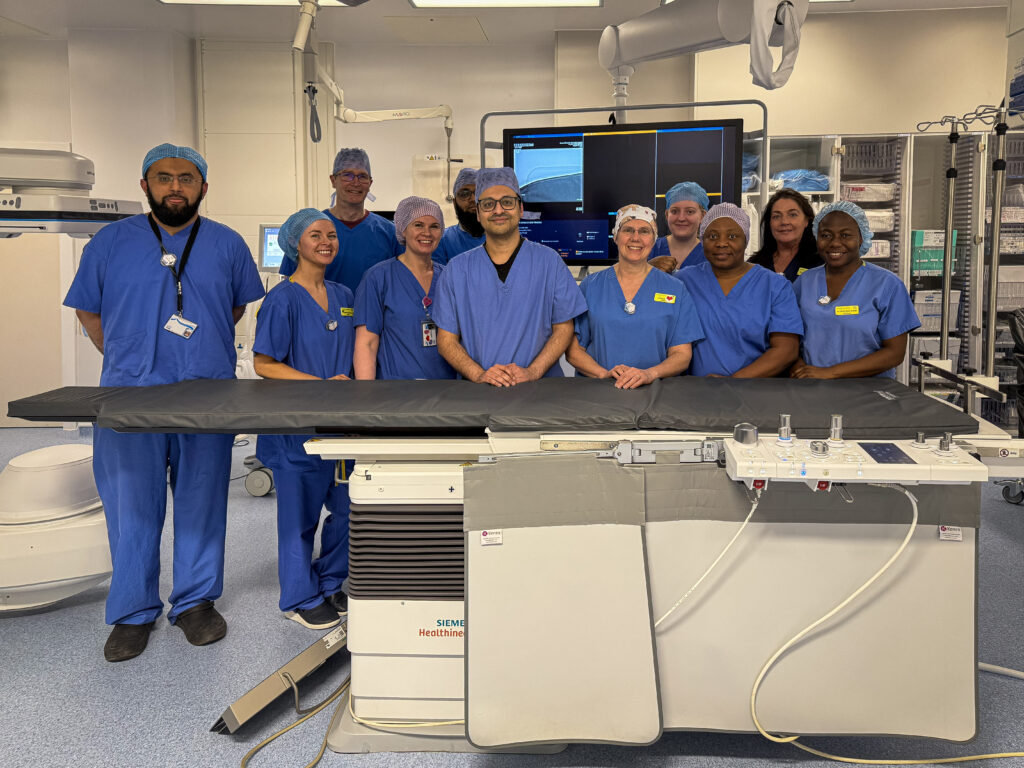 11 members of the thrombectomy team, standing next to an operating table in the Thrombectomy Suite at the Institute of Neurological Sciences