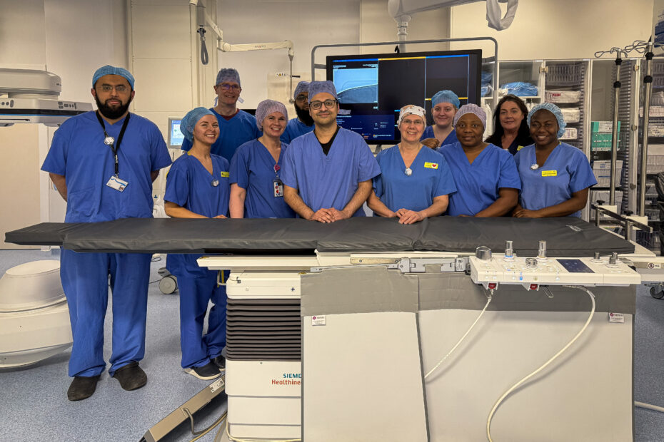 11 members of the thrombectomy team, standing next to an operating table in the Thrombectomy Suite at the Institute of Neurological Sciences